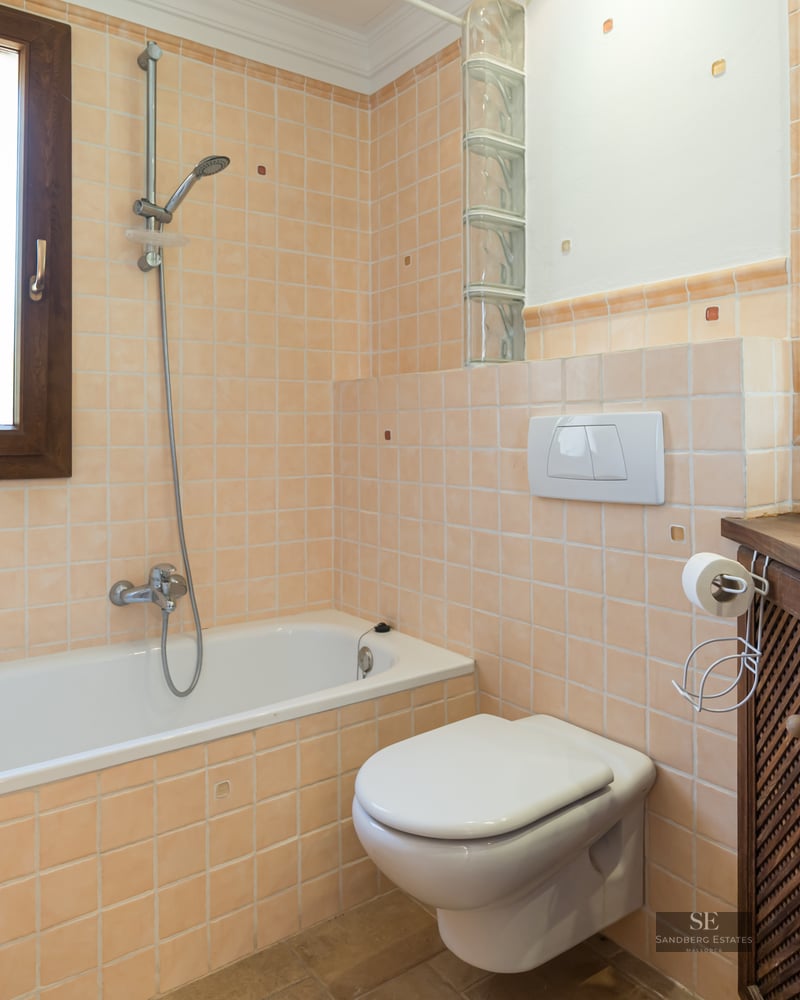 Bathroom featuring peach tiling, a bathtub, wall-hung toilet, and a dark wood vanity unit.