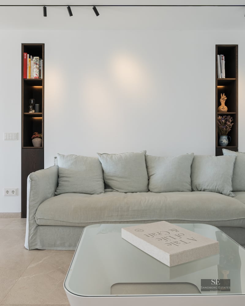 Modern living room featuring a sage green sectional sofa, glass coffee table, and dark wood built-in wall niches.