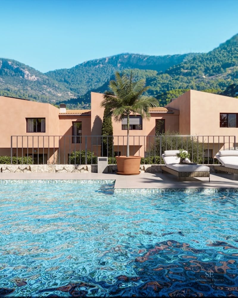 Crystal blue pool with sun loungers in front of terracotta villas and lush green mountains.