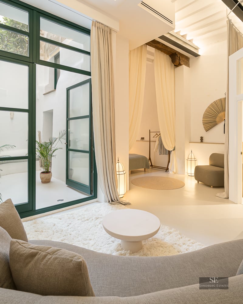 Salon moderne avec un canapé gris incurvé, un tapis à poils longs et de grandes portes vitrées ouvrant sur un patio.