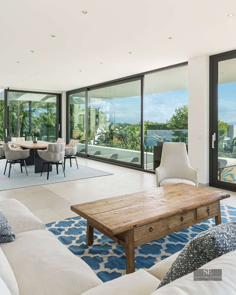 Spacious living room with white sofas, wooden coffee table, and large glass doors opening to a sea-view terrace.