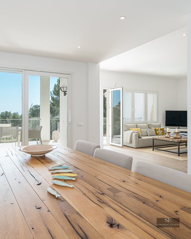 Grande table à manger en bois rustique dans une pièce moderne et lumineuse avec accès à une terrasse panoramique.