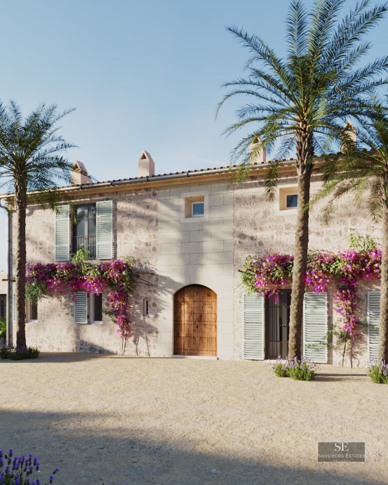 Facade of a rustic stone villa with three palm trees, purple bougainvillea, and a large arched wooden door.