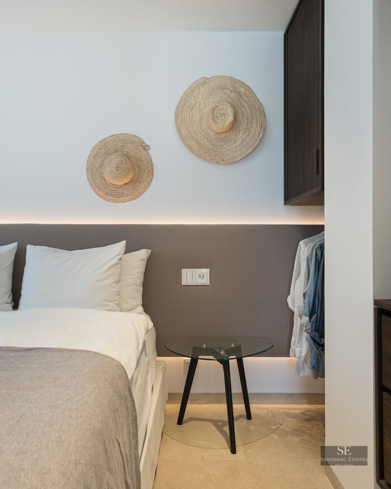 Modern bedroom featuring a backlit headboard, white linens, and decorative straw hats on the wall.