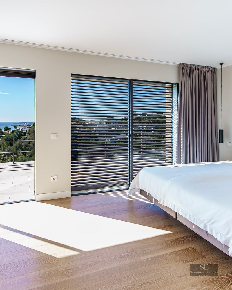 Bright modern master bedroom with large glass doors opening to a terrace overlooking the sea.