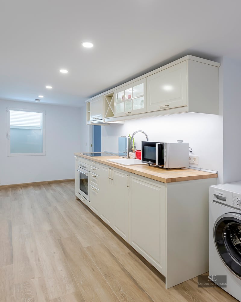 Bright modern kitchen with white cabinets, light wood countertops, and integrated washing machine and dryer.