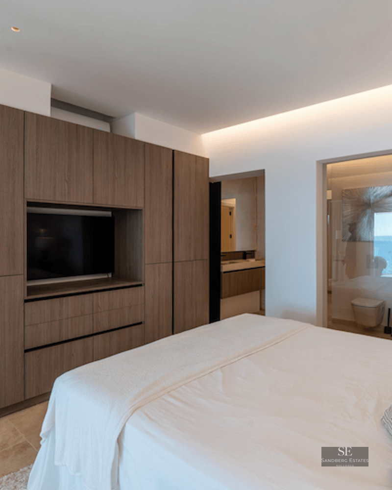 Modern bedroom featuring a large wood closet with integrated TV and a glass-walled ensuite bathroom with sea view.