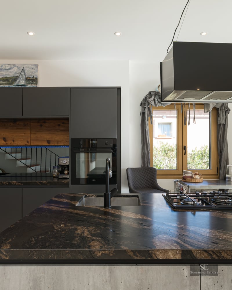 Modern kitchen with dark marble island, matte black cabinetry, and wood accents.