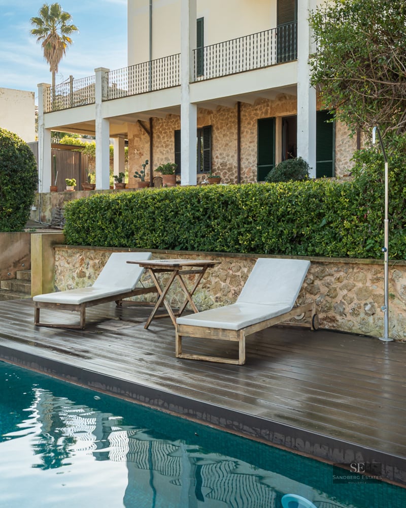 Turquoise swimming pool with dark wood deck, sun loungers, and a rustic stone villa in the background.