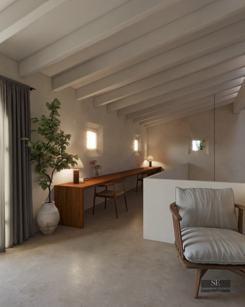 A mezzanine workspace featuring a long wooden desk, exposed white ceiling beams, and a stylish lounge chair by a balcony.