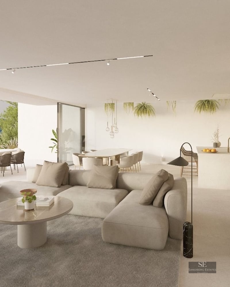 Sunlit minimalist living room with beige sofa, marble tables, and large windows opening to a terrace with sea views.