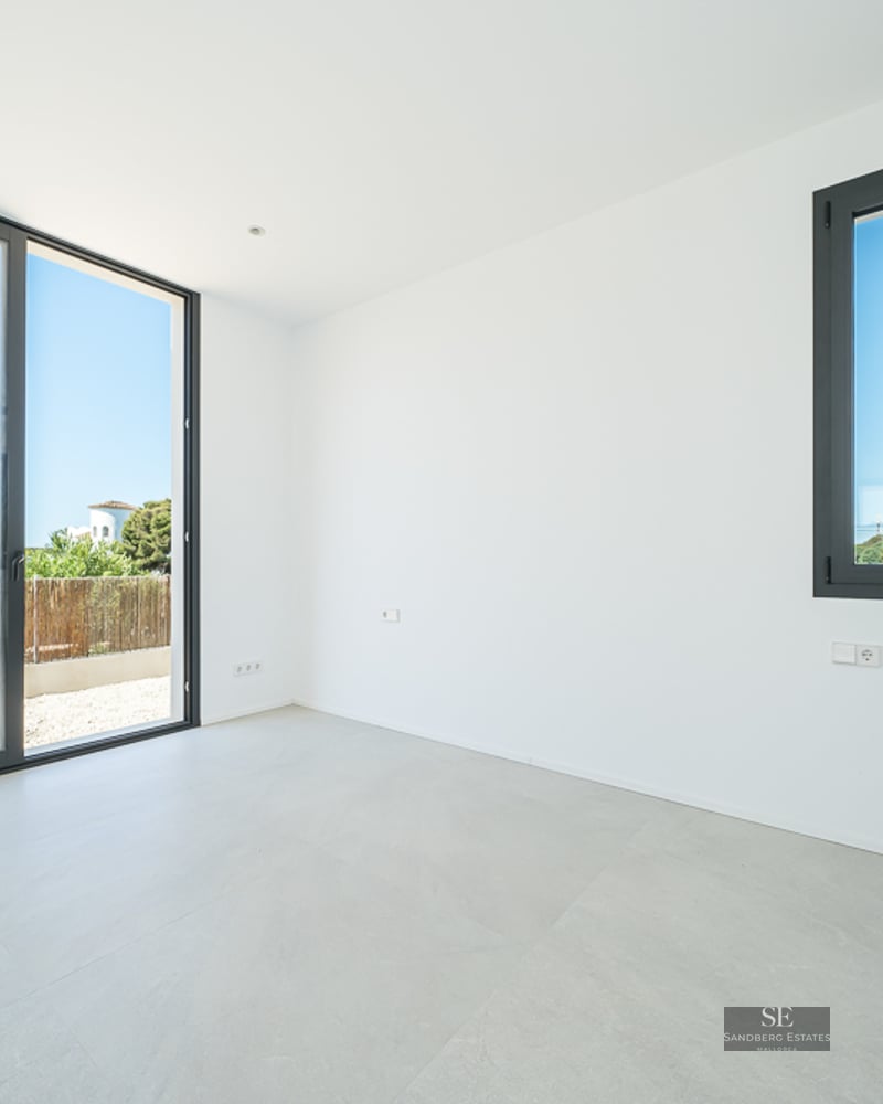 Empty modern room with white walls, grey tile flooring, and a large sliding glass door leading to a patio.
