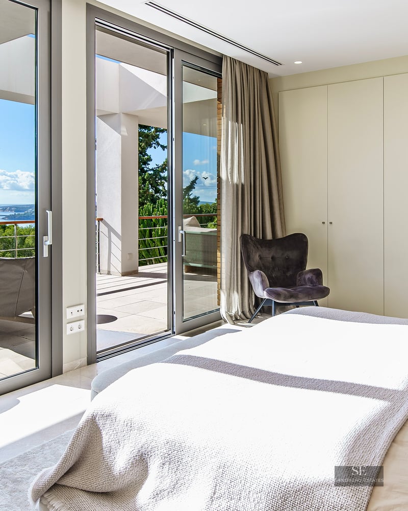 Chambre principale lumineuse avec de grandes baies vitrées ouvrant sur une terrasse ensoleillée avec vue sur la mer.
