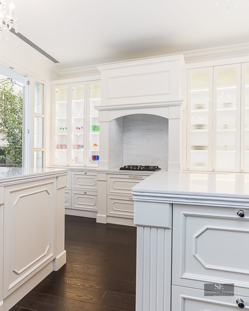 Elegant kitchen featuring white cabinetry, marble countertops, a central island, and a crystal chandelier.