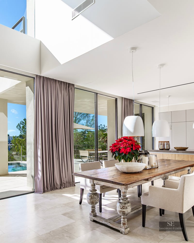 Modern open-plan dining room with a rustic wooden table and glass walls overlooking an infinity pool and valley.