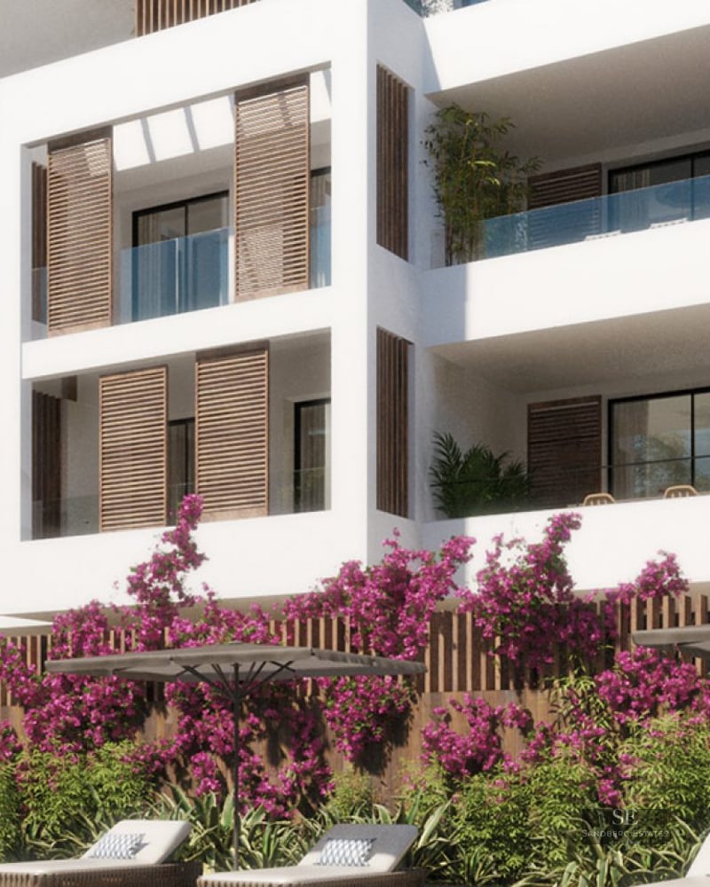 White modern building with wooden shutters, glass balconies, and pink bougainvillea flowers by a lounge area.