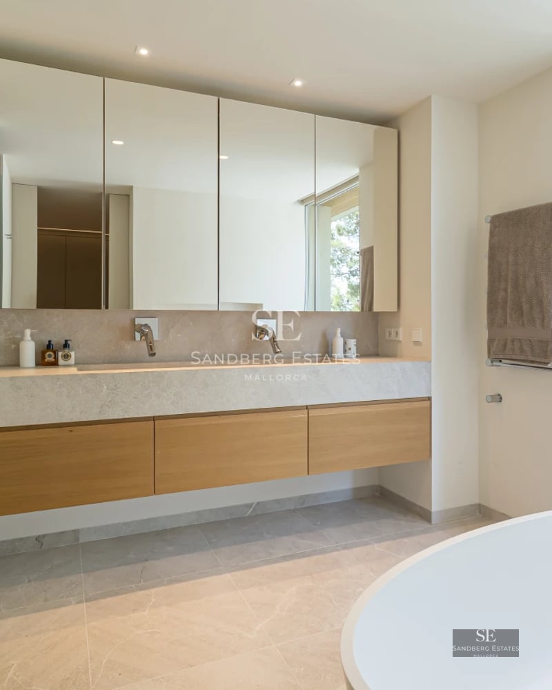 View of the pool and terrace with sun loungers, surrounded by lush greenery and modern architecture. Bright interior visible.