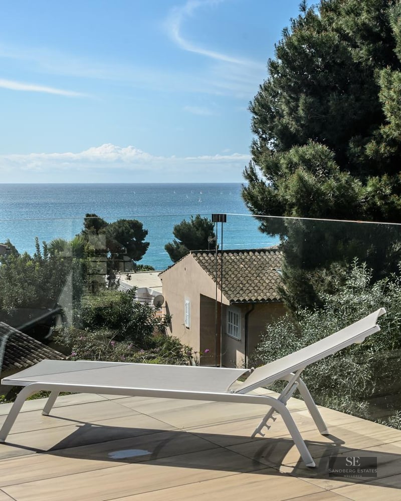 White sun lounger on a modern terrace with a glass railing overlooking the Mediterranean sea.