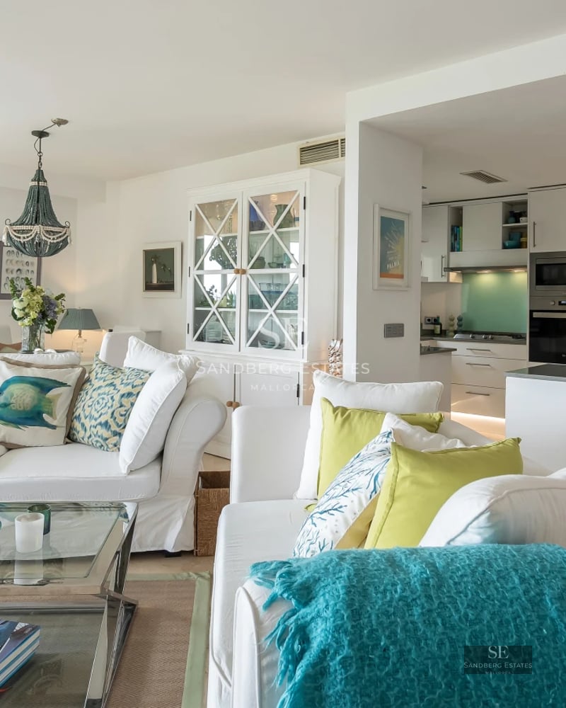 View of an infinity pool with lounge chairs and a modern house featuring large windows and a lush garden in the background.