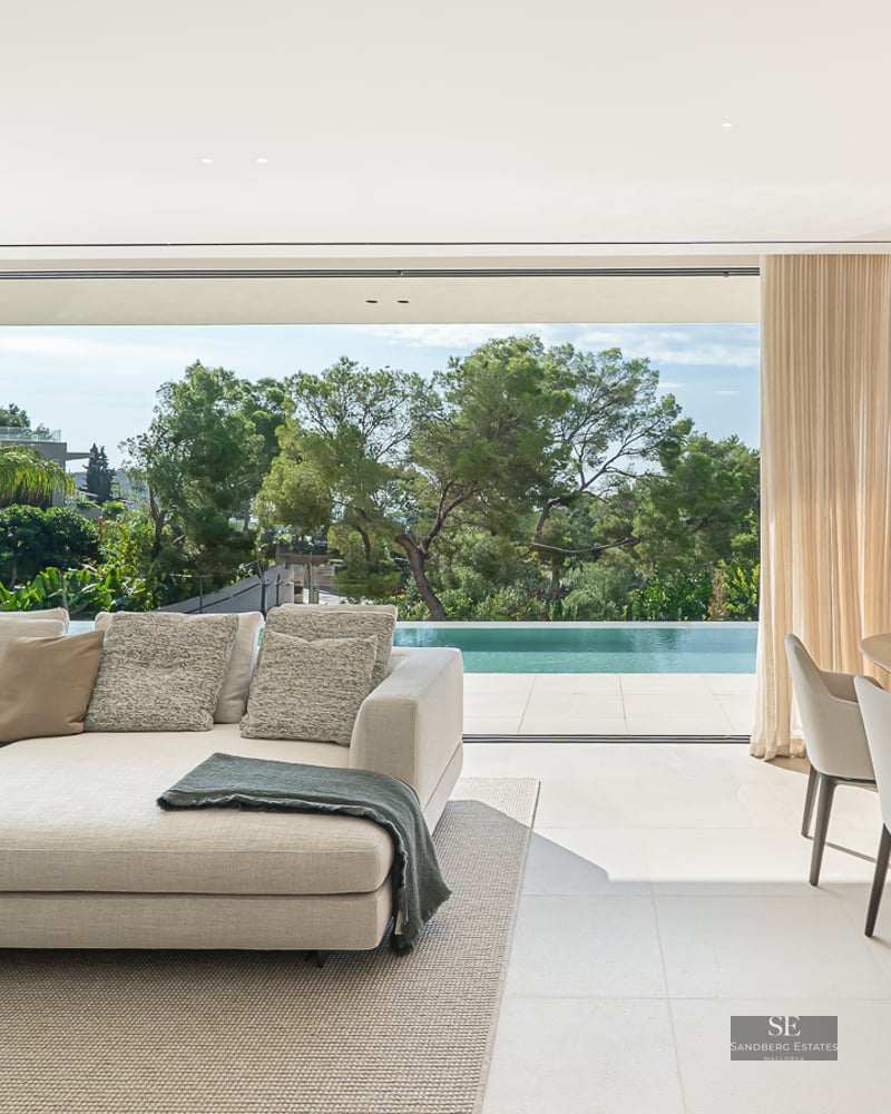 Elegant modern living room featuring a beige sectional, dining set, and large sliding doors opening to a pool terrace.