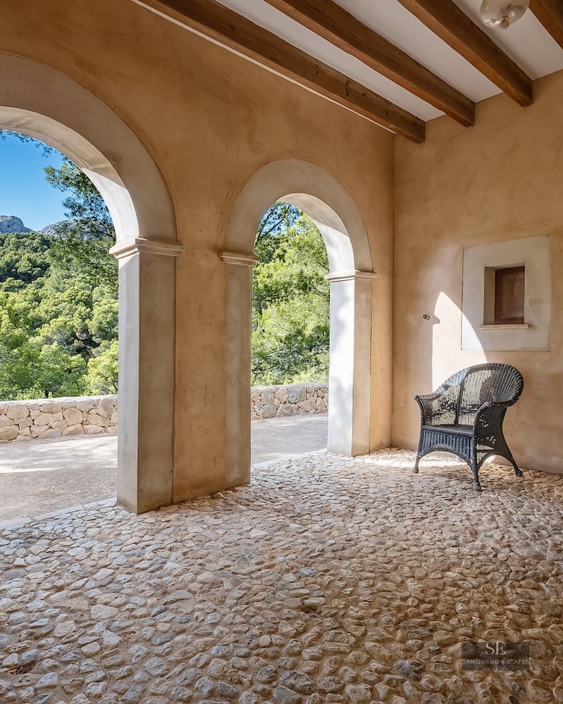 Rustic terrace featuring stone arches, wooden beams, cobblestone flooring, and a scenic mountain forest view.
