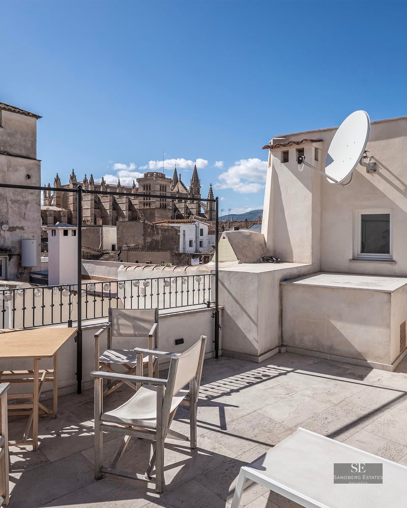 Toit-terrasse spacieux avec mobilier en bois et vue imprenable sur la cathédrale historique sous un ciel bleu.