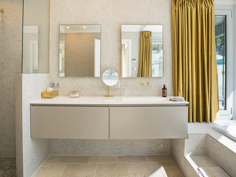 Modernes Badezimmer mit beigem schwebendem Doppelwaschtisch, zwei Spiegeln und goldfarbenen Vorhängen.