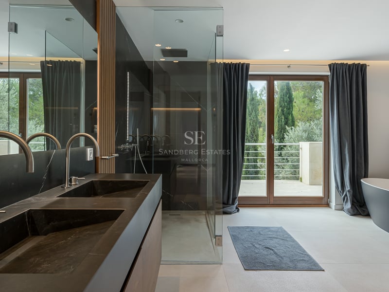 Salle de bains moderne avec double vasque noire, douche à l'italienne, baignoire îlot et vue sur la forêt.