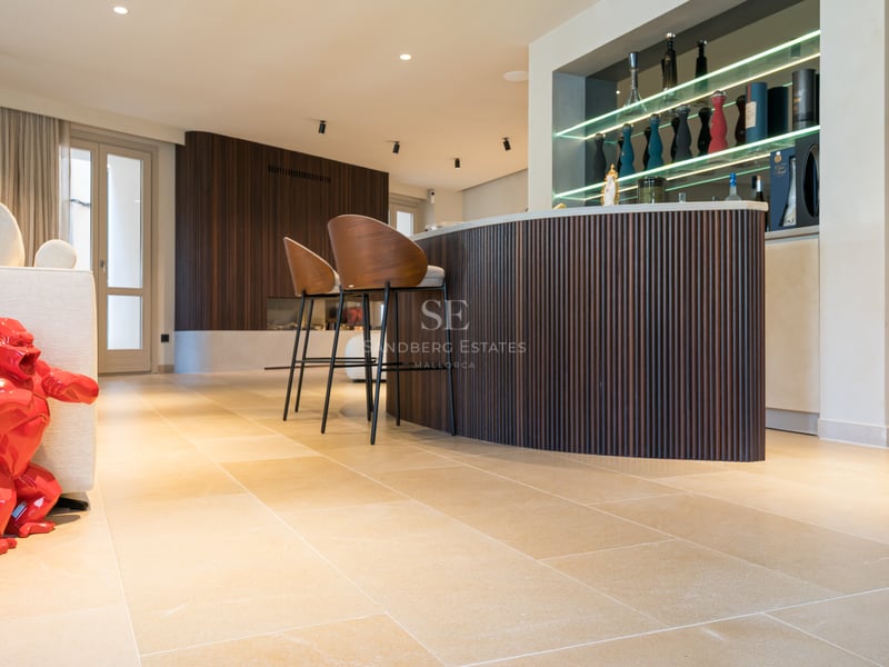 Bar contemporain avec boiseries rainurées, tabourets en cuir et sol en pierre dans une villa de luxe.