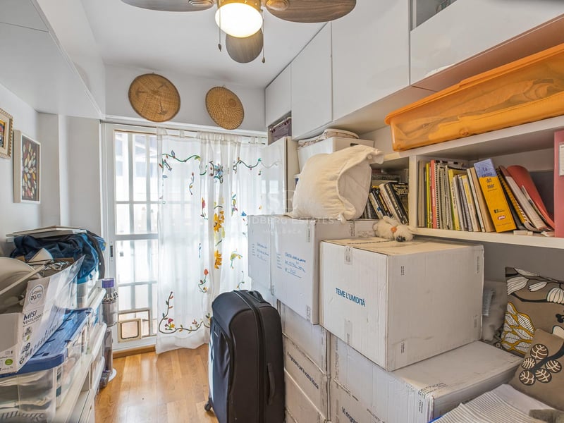 Ein kleiner Raum mit weißen Einbauschränken, Regalen, Umzugskartons, einem Deckenventilator und natürlichem Licht.