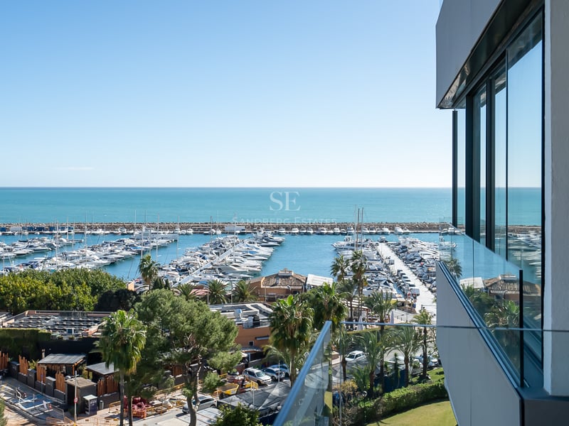 Erhöhte Ansicht von einem modernen Balkon über einen Yachthafen und das Mittelmeer unter klarem blauem Himmel.