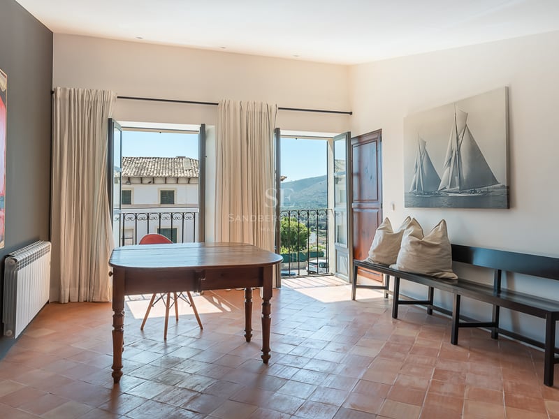 Pièce lumineuse avec sol en terre cuite, table en bois rustique et portes-fenêtres ouvrant sur le paysage.