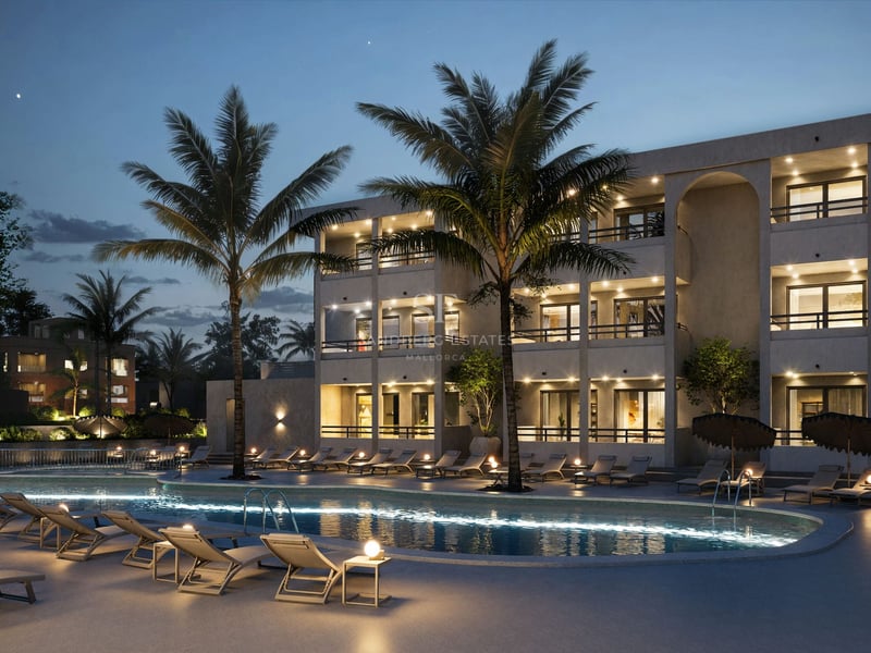 Grande piscine illuminée avec chaises longues et palmiers devant un immeuble d'appartements moderne au crépuscule.