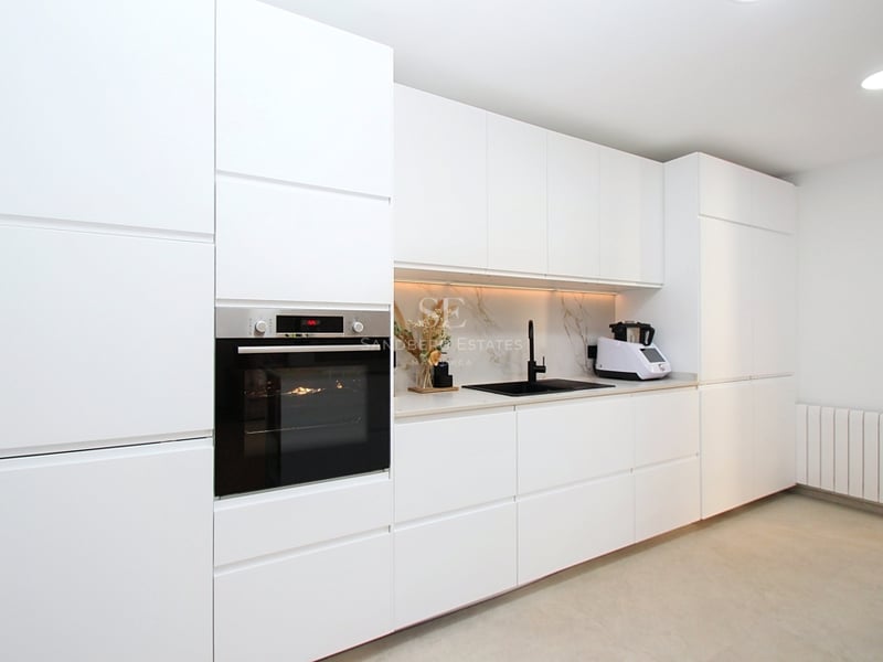 Modernt vitt kök med handtagsfria skåp, svart kran och integrerad ugn i rostfritt stål.