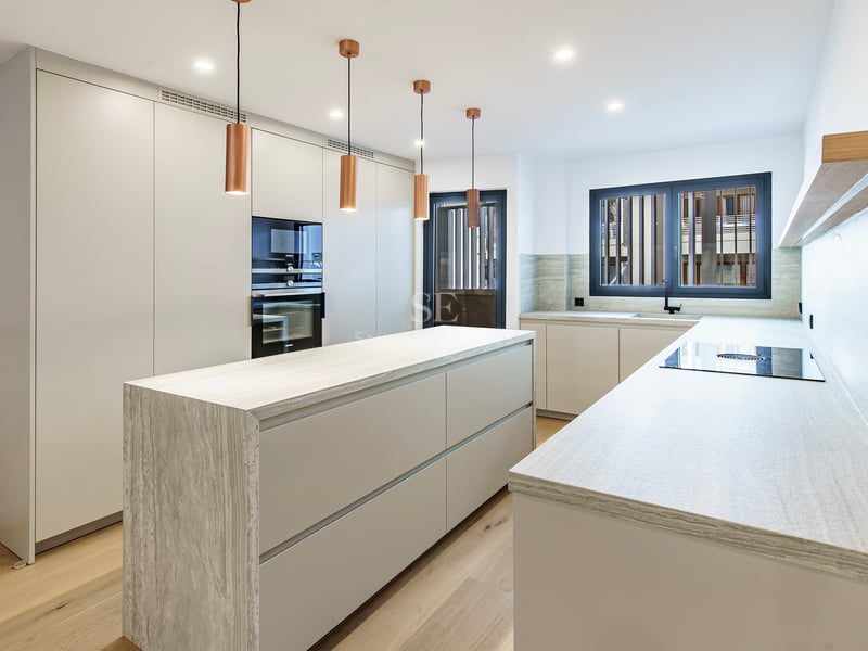 Cuisine contemporaine blanche avec îlot en pierre, suspensions en cuivre et parquet en bois.