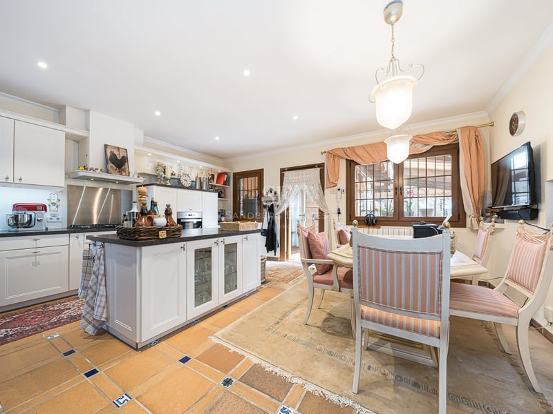 Grande cuisine avec meubles blancs, îlot central, sol en terre cuite et coin repas avec chaises rayées.