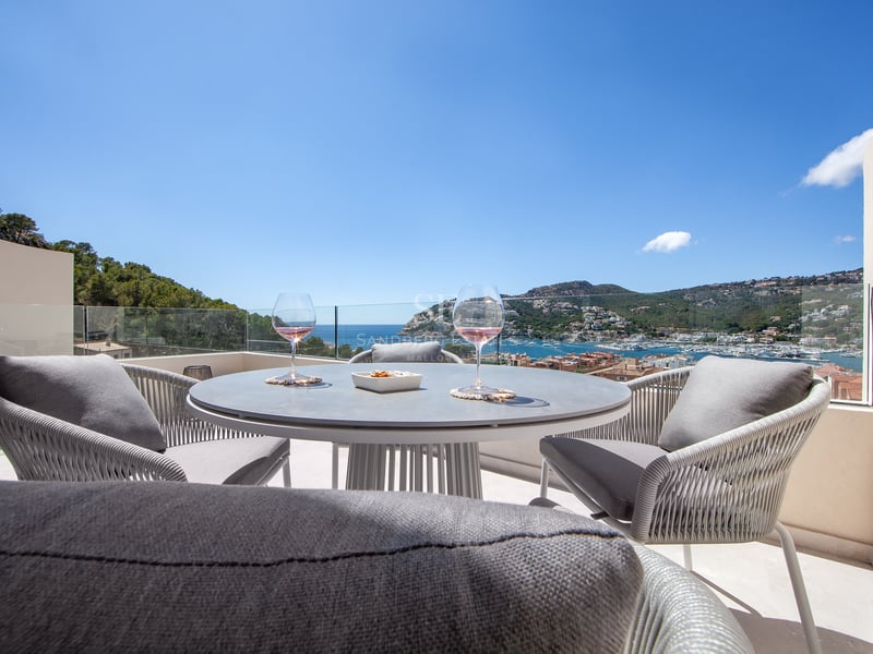 Table de terrasse moderne avec deux verres de vin devant une vue imprenable sur le port et la mer par temps clair.