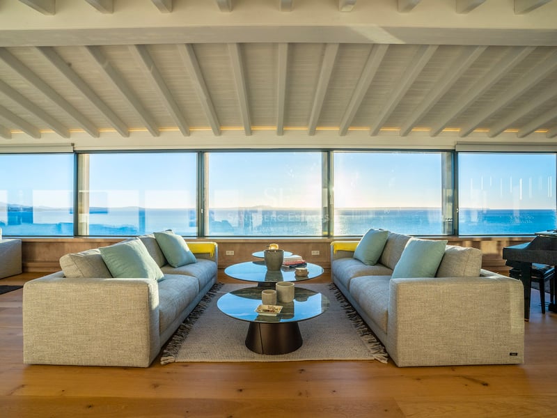 Modernes Wohnzimmer mit grauen Sofas, Glastischen und bodentiefen Fenstern mit Blick auf das Mittelmeer.