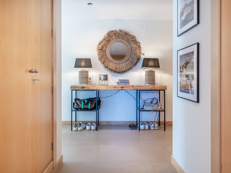 Couloir avec console en bois brut, miroir soleil en fibres et lampes en corde sur sol clair.