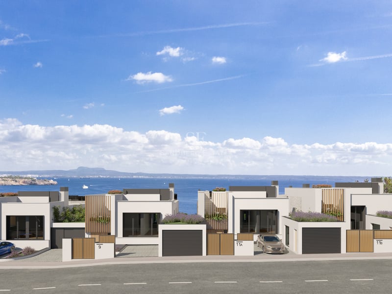 Row of modern white villas with wooden accents and green roofs overlooking the sea under a blue sky.