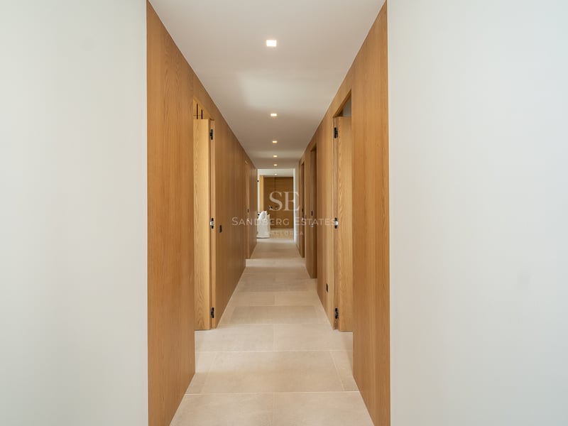 Couloir symétrique avec panneaux muraux en chêne clair, sol en pierre naturelle et éclairage encastré au plafond.