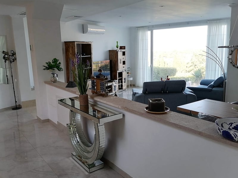 Salon moderne avec sol en marbre, canapés bleus et grande baie vitrée donnant sur un jardin verdoyant.