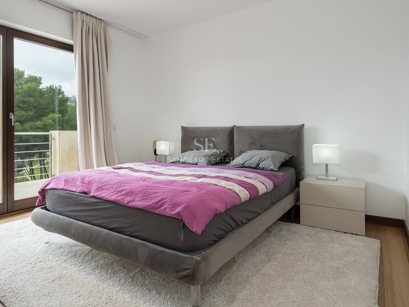 Chambre contemporaine avec lit rembourré gris, couette prune, tapis blanc et porte-fenêtre donnant sur un balcon.