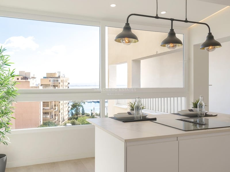 Weiße Kücheninsel mit Induktionskochfeld vor einem großen Fenster mit Blick auf den Hafen und die Stadt.
