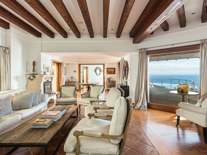 Grand balcon avec vue sur mer depuis un appartement moderne. Garde-corps en verre, plancher en bois et mobilier extérieur élégant.