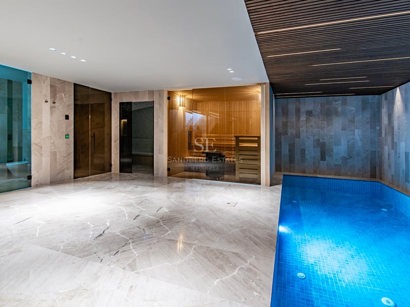 Spa intérieur avec petite piscine bleue, sauna vitré et sol en marbre sous un plafond à lattes.