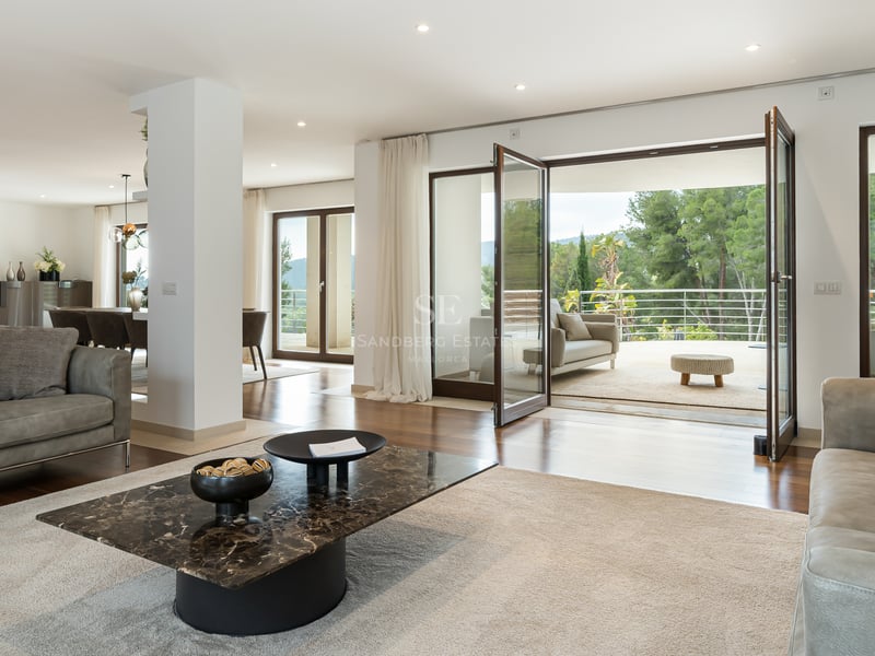 Salon moderne avec canapés en cuir, table en marbre et grandes baies vitrées ouvrant sur une terrasse vue forêt.