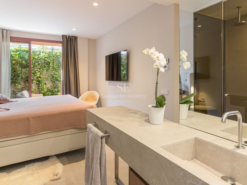 A modern master bedroom featuring a natural stone vanity and sink, a large mirror, and access to a green patio.