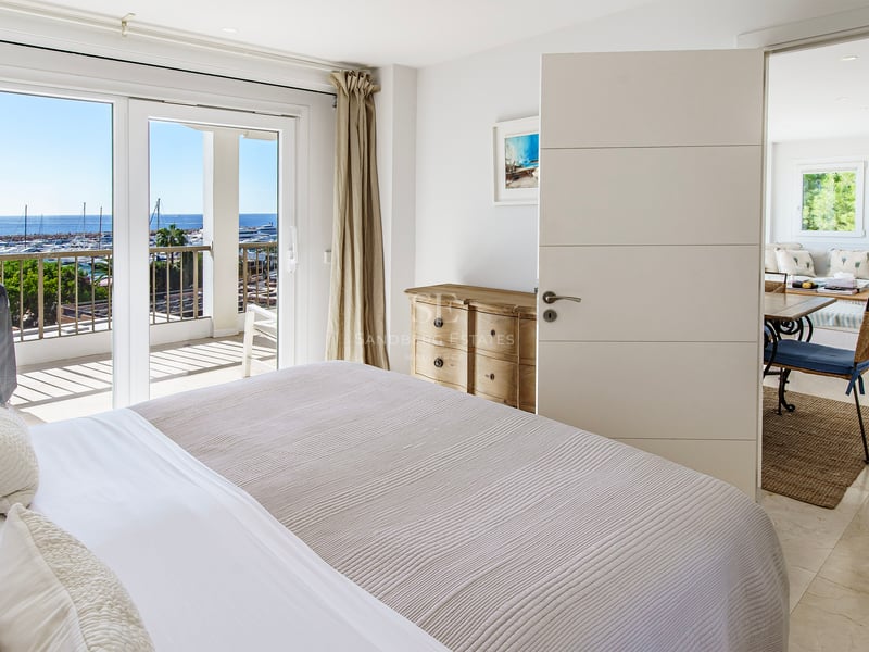 Bright bedroom featuring a large bed, sliding doors to a terrace, and panoramic views of a marina.
