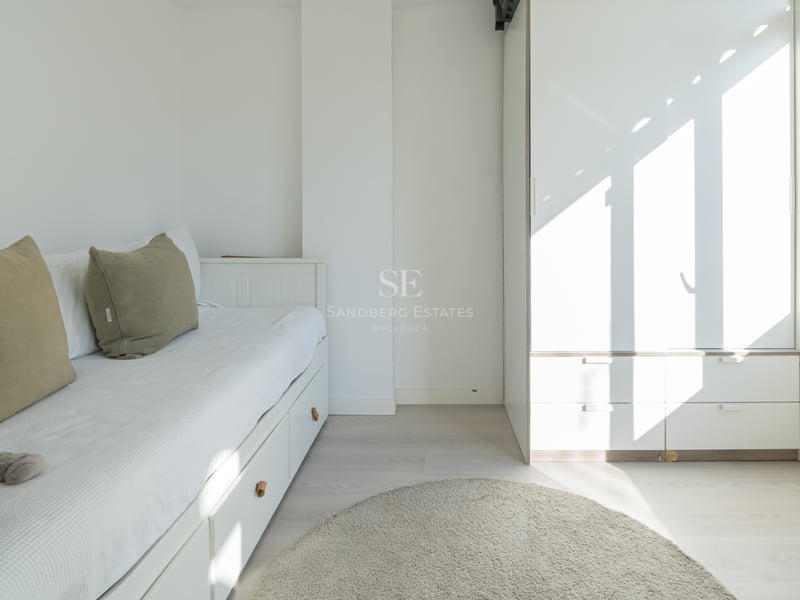 Bright white bedroom with a trundle bed, olive green pillows, large wardrobe, and a round grey rug.